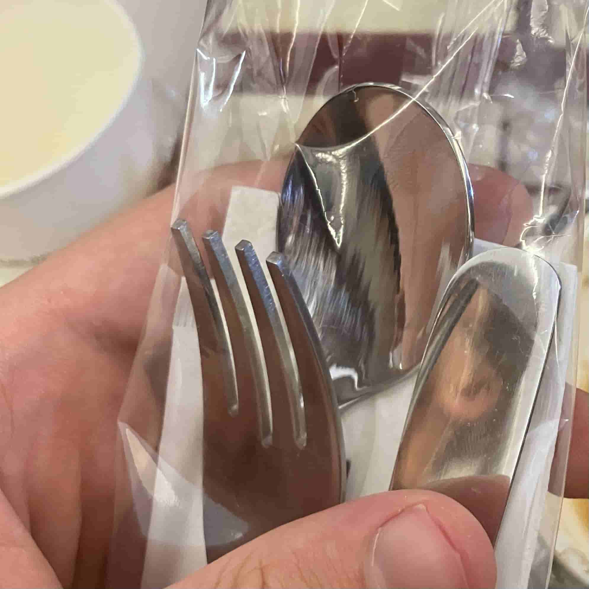 My hand holding metal utensils sealed in plastic packaging